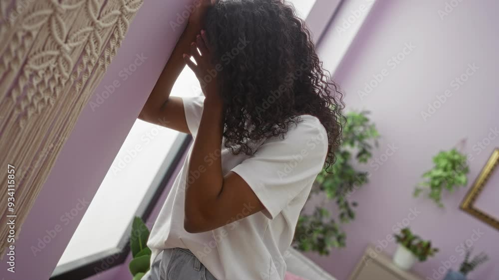 Young african american woman with curly hair feeling dizzy and leaning on a purple wall in an indoor home setting with plants in the background. Young african american woman with curly hair feeling dizzy and leaning on a purple wall in an indoor home setting with plants in the background.