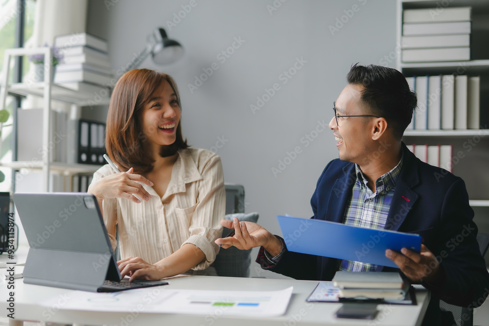Two business people discussing happily while working together over a digital tablet and business documents in the office Two business people discussing happily while working together over a digital tablet and business documents in the office