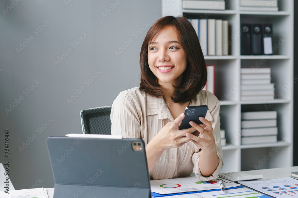 Young businesswoman is smiling while using her smartphone at her desk in a modern office Young businesswoman is smiling while using her smartphone at her desk in a modern office