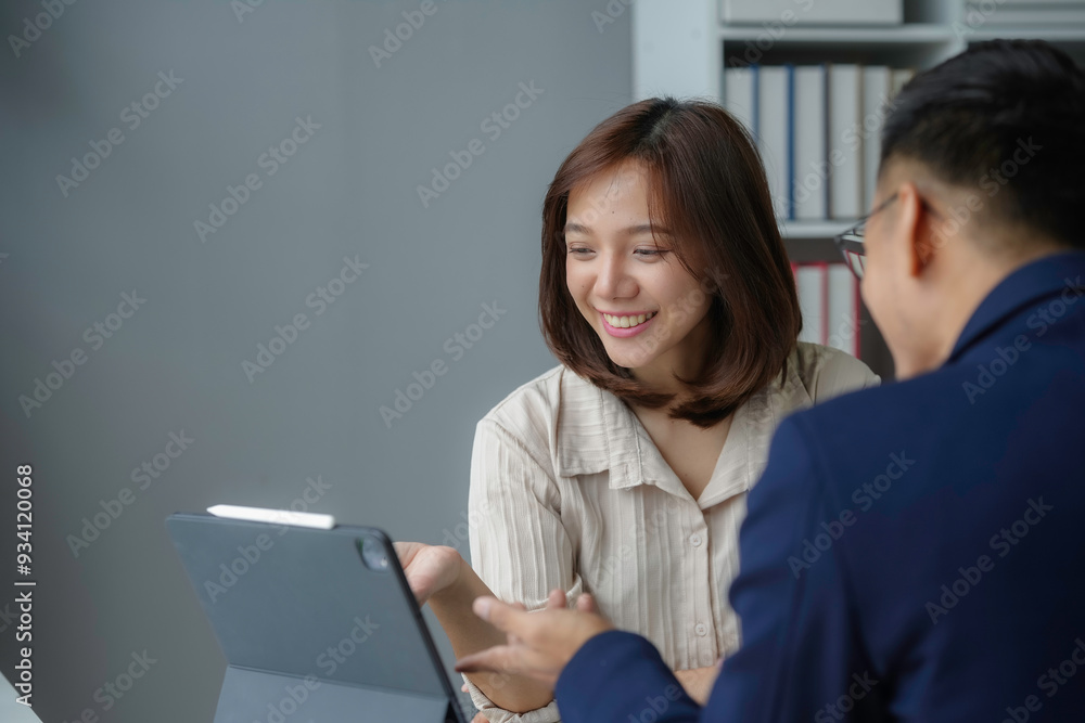 Two asian business people smiling and looking at a tablet computer while working together in the office Two asian business people smiling and looking at a tablet computer while working together in the office