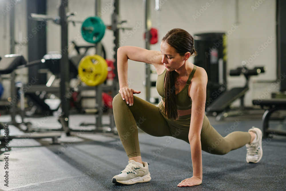 Toned female athlete practicing static stretching in fully equipped gym Toned female athlete practicing static stretching in fully equipped gym
