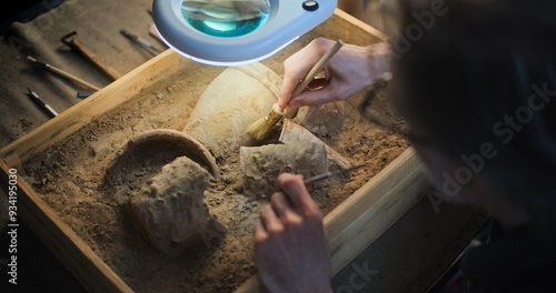 Foto Close up of mature archaeologist cleaning cultural heritage of extinct civilization from sand under lamp, using brush