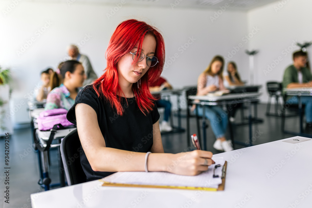 Fototapeta premium Focused young student taking notes from books for her study. College student sitting at desk and studying.