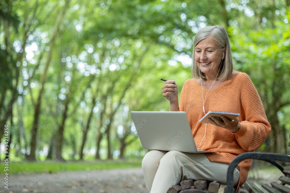 Obraz premium Smiling woman learning online in a serene outdoor environment using laptop and notebook. Capturing knowledge and nature, she enjoys the synergy of technology and tranquility for productive learning.