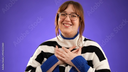 Young smiling good kind surprised happy woman 20s wear jumper ask who me oh it so sweet put hands on chest isolated on purple background studio portrait. People lifestyle concept photo