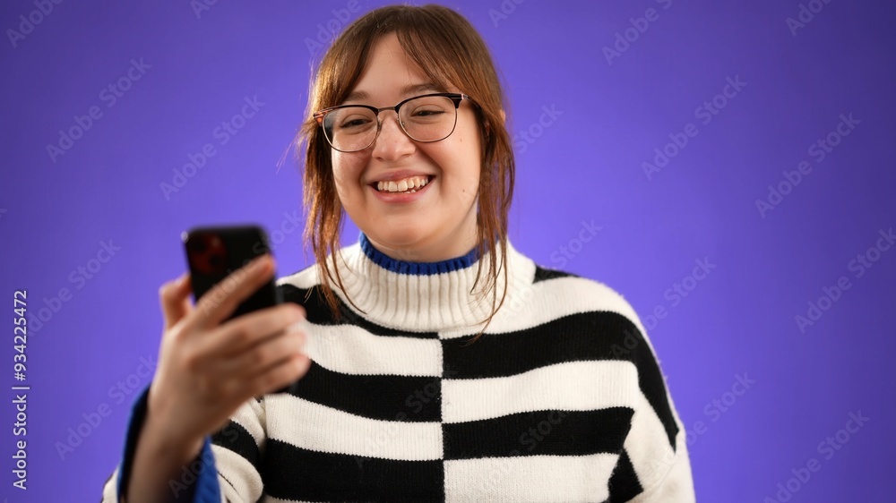 Woman 20s, wearing sweater waving and having a video chat consultation with a friend or doctor on the phone, webcam isolated on purple background. Woman 20s, wearing sweater waving and having a video chat consultation with a friend or doctor on the phone, webcam isolated on purple background.