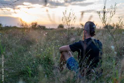 A young man with a beard and a mohawk in a field at sunset.