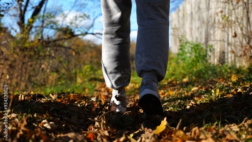 Close up to male feet in sneakers going along trail on fallen dry leaves. Legs of young man stepping along path outdoor. Guy walking at nature sunny autumn day. Low view Slow mo