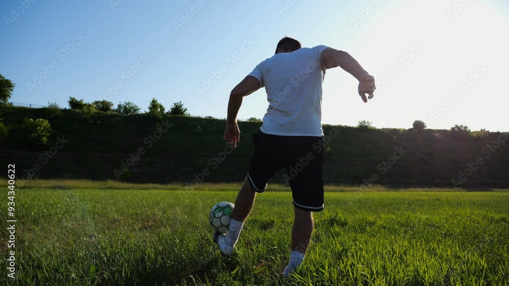 Sportsman juggling soccer ball on stadium at sunny day. Young man kicking ball at green field. Professional footballer practicing tricks at meadow with sunlight at background. Freestyle football. Sportsman juggling soccer ball on stadium at sunny day. Young man kicking ball at green field. Professional footballer practicing tricks at meadow with sunlight at background. Freestyle football.