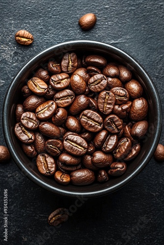 Freshly roasted coffee beans in a black bowl on a textured dark surface