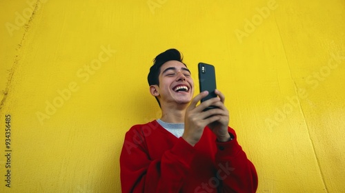 Young person smiling while using a smartphone against a bright yellow wall in...