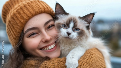 Young woman in a yellow sweater joyfully cuddles her striped cat outdoors on ...