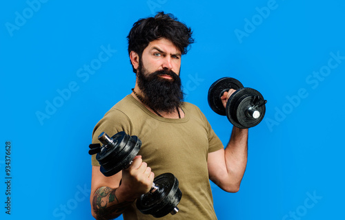 Serious man in sportswear raising dumbbells. Muscular bearded man with dumbbells during an exercise. Strong sportsman does weightlifting. Handsome male fitness model athlete lifting dumbbells in gym.