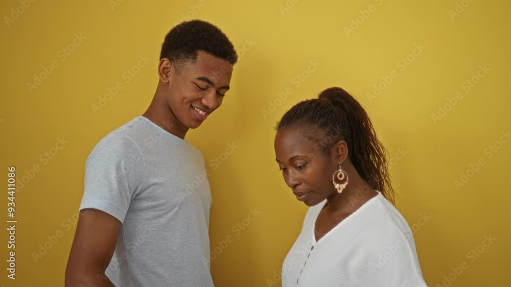 Mother and son making a heart gesture with their hands against a yellow background, showcasing their black, african american culture, family bond, and love together in an isolated setting. Mother and son making a heart gesture with their hands against a yellow background, showcasing their black, african american culture, family bond, and love together in an isolated setting.