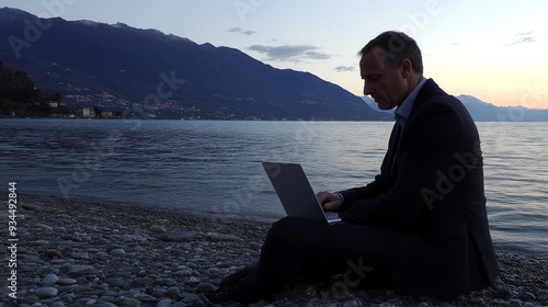 Digital nomad freelancer working by the blue lake Como at golden hour, Italy. Flexible workplace culture. Travelling man on laptop outdoors, scenic view. Copy space.