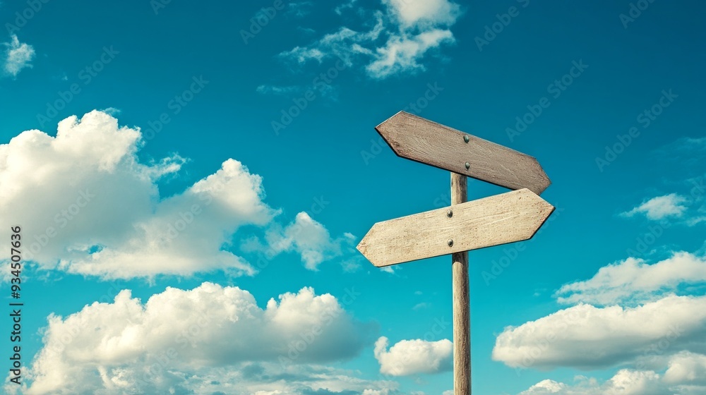 A pair of wooden directional signs stands against a bright blue sky filled with fluffy clouds. The signs point in different directions, suggesting choices A pair of wooden directional signs stands against a bright blue sky filled with fluffy clouds. The signs point in different directions, suggesting choices