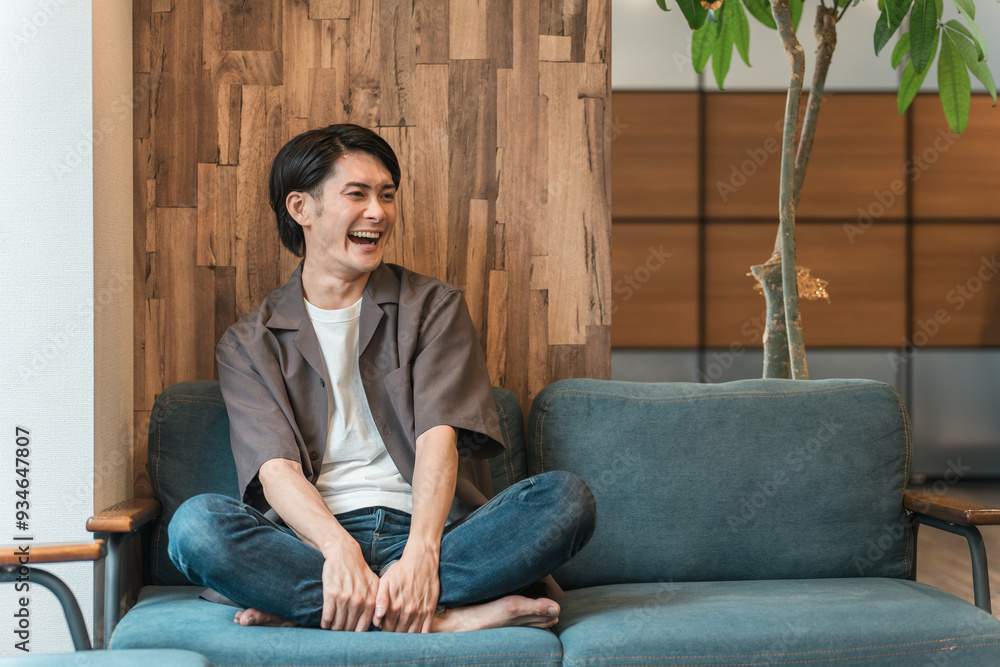 家のリビングでくつろぐ笑顔の若いアジア人・日本人男性（リラックス）
