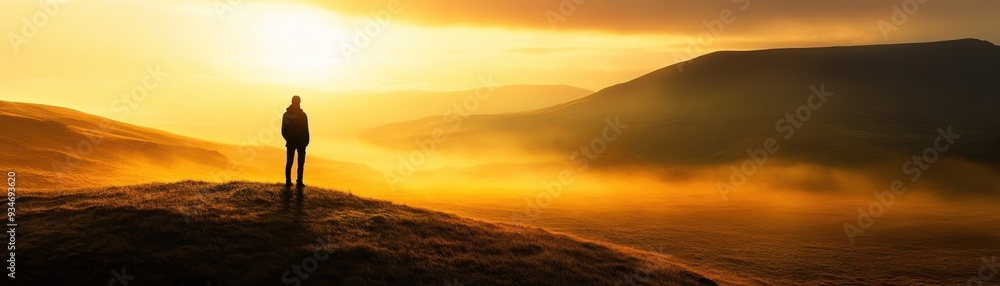 Silhouette of a Person Standing on a Hill During a Golden Sunrise with Misty Mountains in the Background Silhouette of a Person Standing on a Hill During a Golden Sunrise with Misty Mountains in the Background