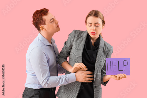 Vászonkép Business woman holding paper with word HELP and her male colleague on pink background