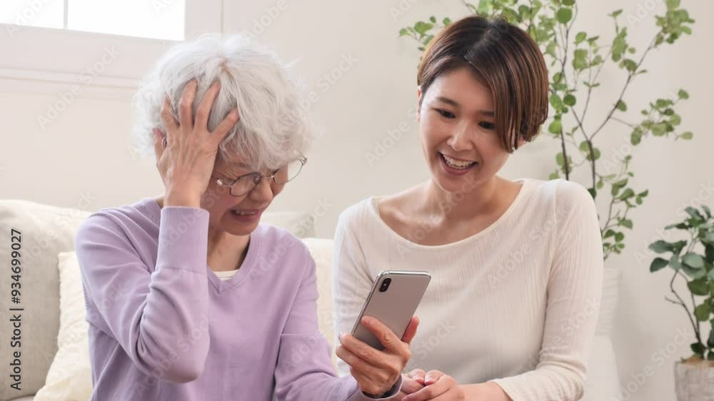 母親にスマートフォンの操作を教える娘 リビングルーム 母親にスマートフォンの操作を教える娘 リビングルーム
