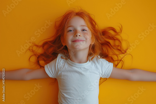 Happy redheaded child in white t-shirt laying on yellow background