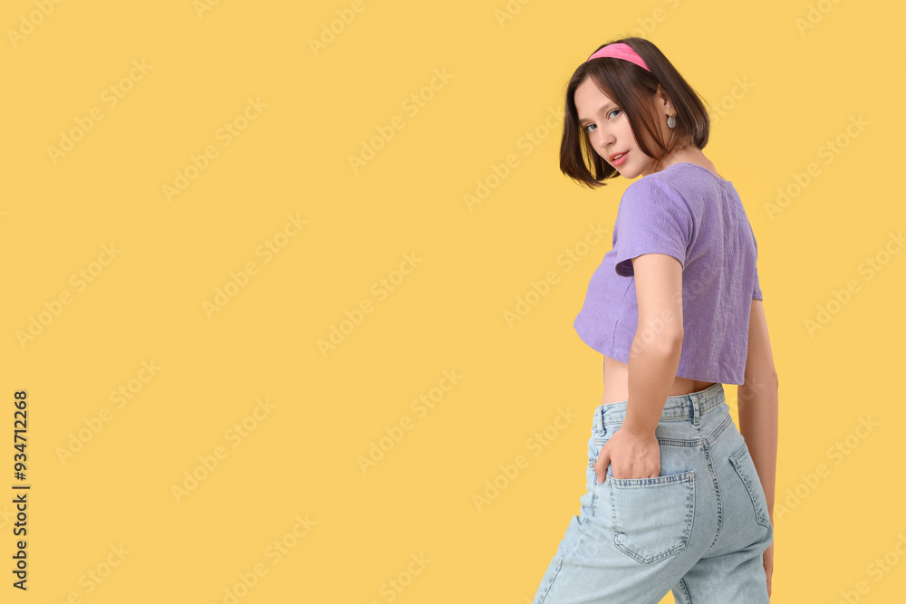 Beautiful young woman in stylish jeans on yellow background