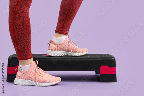 Female legs in sneakers with stepper on lilac background photo