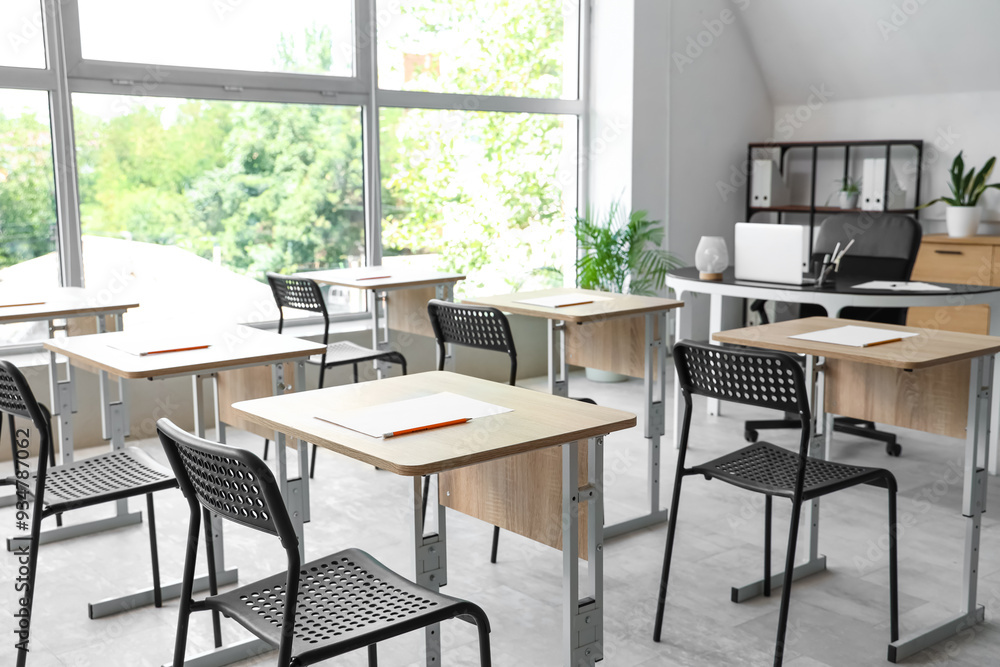 Fototapeta premium Desks with papers and chairs in empty classroom at school