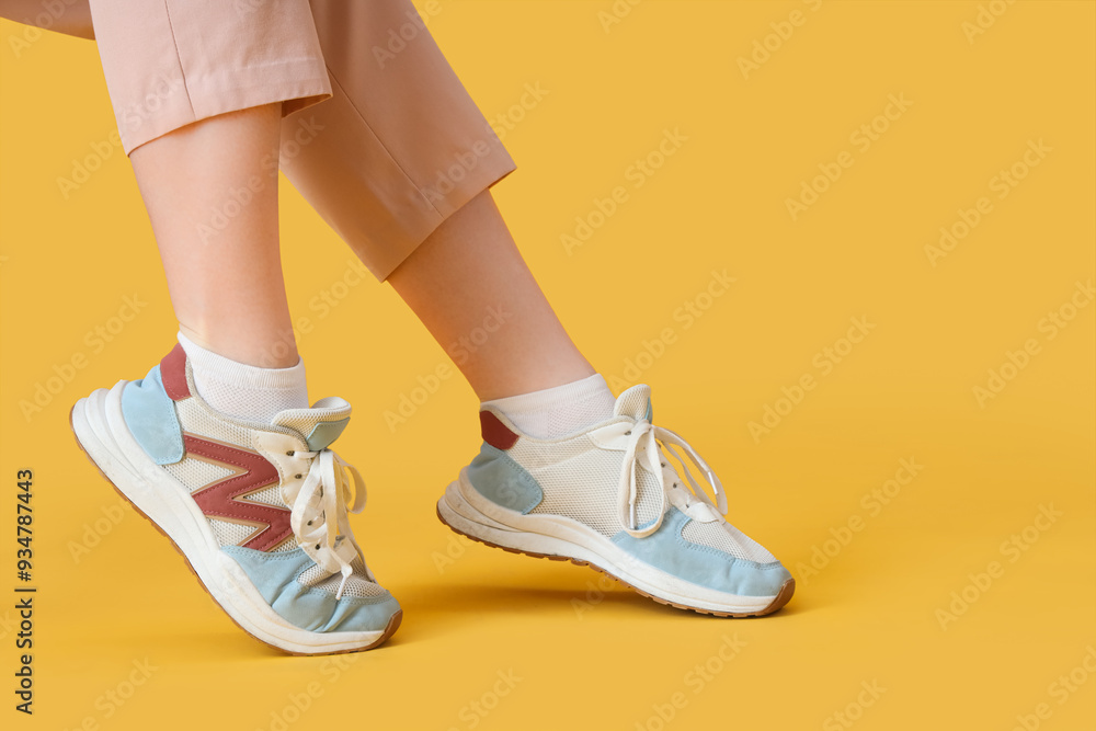 Female legs in sneakers on yellow background Female legs in sneakers on yellow background