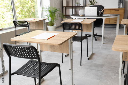 Desks with papers and chairs in modern empty classroom