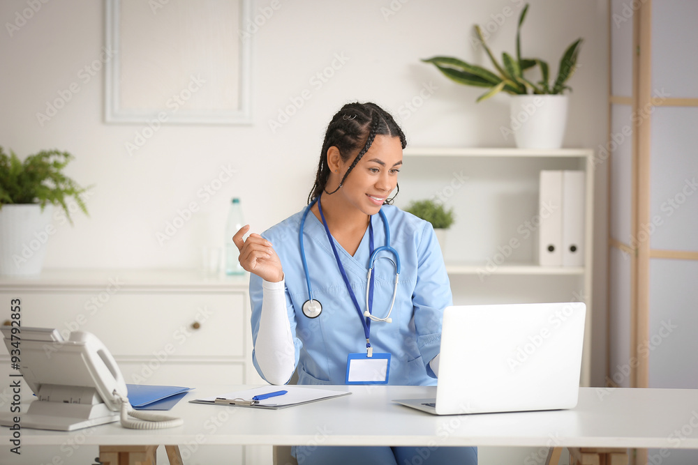 Young African-American female doctor working with laptop at table in clinic Young African-American female doctor working with laptop at table in clinic