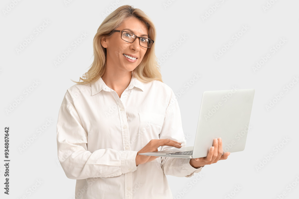 Mature businesswoman in eyeglasses working with laptop on light background Mature businesswoman in eyeglasses working with laptop on light background