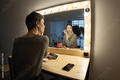 young beautiful woman putting on makeup near the mirror