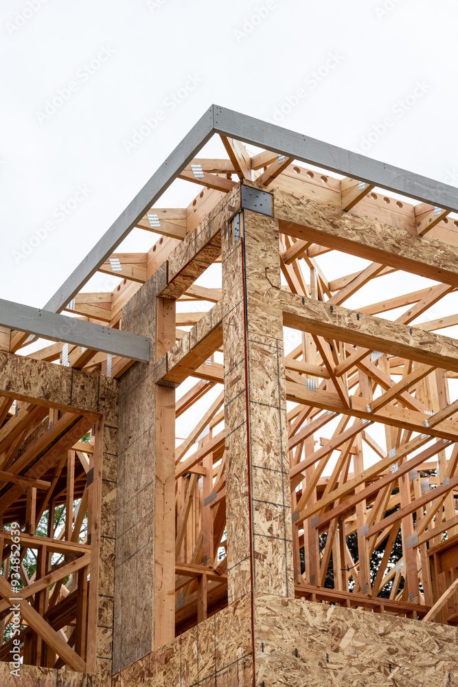 Obraz premium New residential home construction in framing stage, looking up at roof rafter detail through window openings at interior wood stud framing 