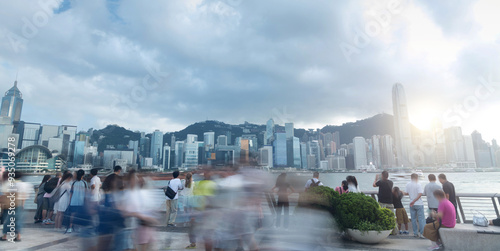 Tourists and citizens enjoying a cloudy day walking on the Hong Kong waterfront, with skyscrapers and victoria bay in the background photo