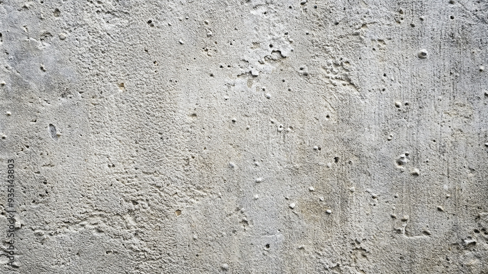 Fototapeta premium The surface of a concrete wall displays a unique texture characterized by bumps, pockmarks, and a mix of soft gray tones, highlighting its age and natural wear patterns over time