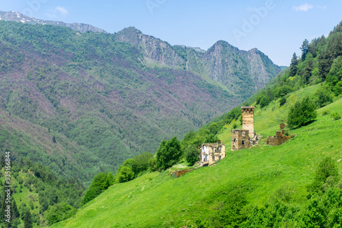 Wallpaper Mural A stone tower with loopholes and the ruins of a dwelling on a steep slope of a green field. High mountains in the background Torontodigital.ca