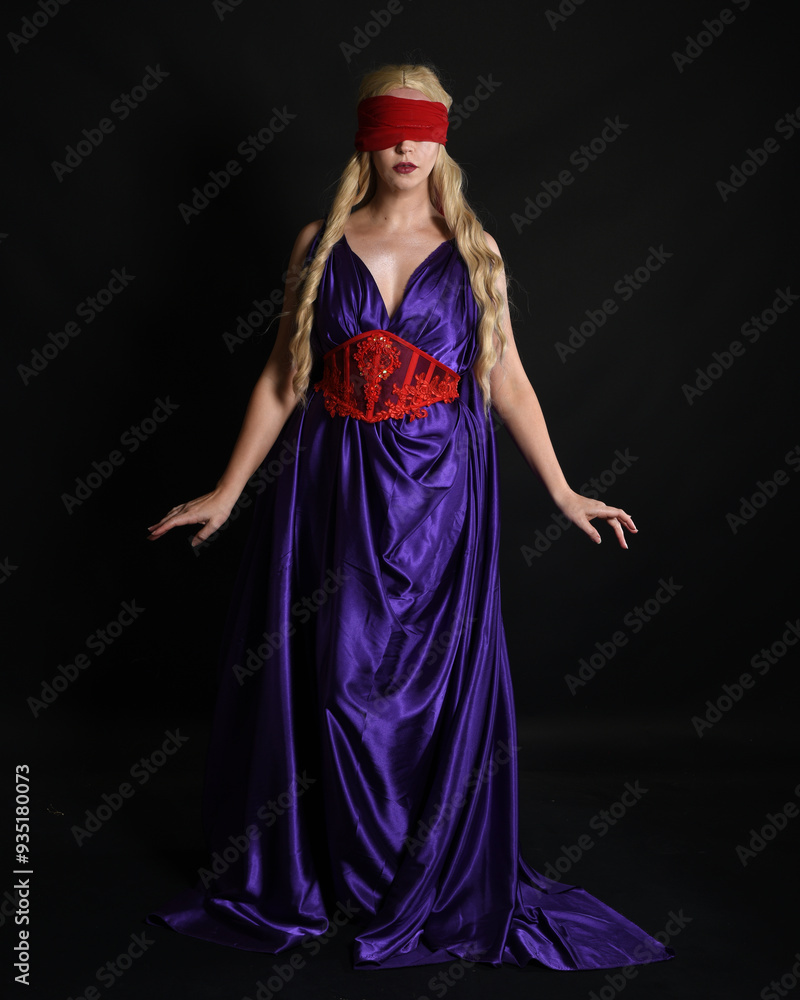 Close up portrait of beautiful blonde female model wearing silk grecian toga dress and red blindfold, historical fantasy goddess, isolated on dark studio background. Close up portrait of beautiful blonde female model wearing silk grecian toga dress and red blindfold, historical fantasy goddess, isolated on dark studio background.