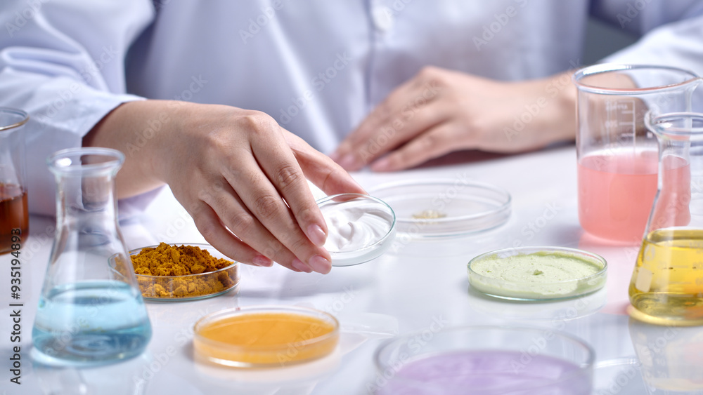 Cosmetic advertising template photo with laboratory concept was shot from close up side view, scientist lift a glass petri dish contains white cream up, several lab glassware scattered lay on table Cosmetic advertising template photo with laboratory concept was shot from close up side view, scientist lift a glass petri dish contains white cream up, several lab glassware scattered lay on table