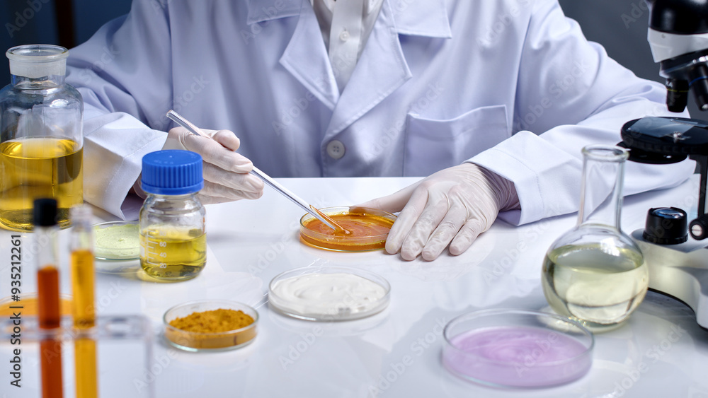 High angle shot photo at a white table top in laboratory, a researcher stirring yellow essence in glass petri dish to do chemical experiment for cosmetics, surrounded with plenty lab instruments High angle shot photo at a white table top in laboratory, a researcher stirring yellow essence in glass petri dish to do chemical experiment for cosmetics, surrounded with plenty lab instruments