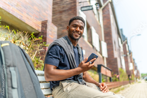 Happy african man using mobile sitting on a street bench