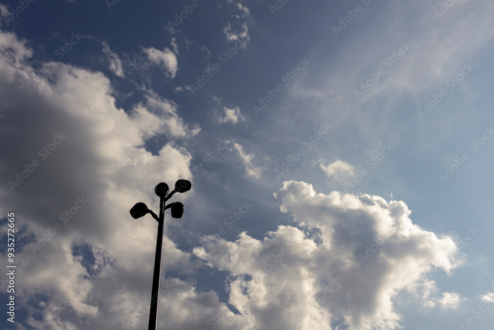 A pole with three lights on top of it is silhouetted against a cloudy sky A pole with three lights on top of it is silhouetted against a cloudy sky