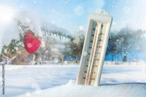  Christmas and New Year weather forecast concept. Weather thermometer measuring Fahrenheit and Celsius stuck in snowdrift, decorated Christmas tree outdoors in background. photo