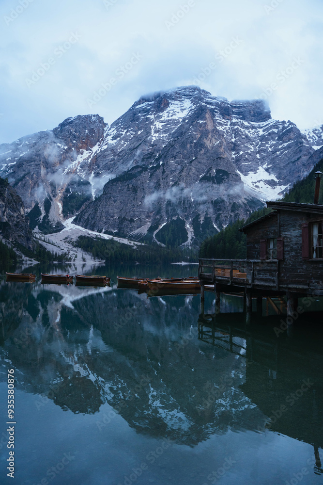Fototapeta premium Turquoise water lake with rowing wood boats surrounded by pine trees and snowed mountains reflected in the Italian Alps, The Dolomites, Italy
