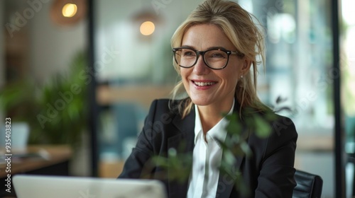 A cheerful businesswoman sits at her desk in a contemporary office, engaging with her laptop and enjoying a productive morning filled with creativity