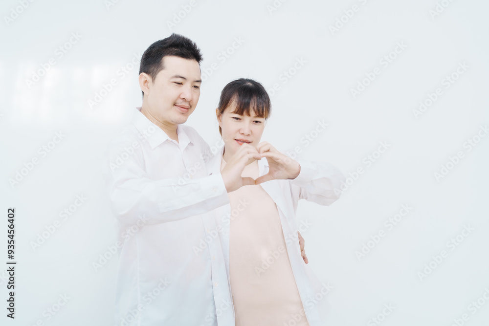 A happy Asian couple, expecting a baby, embraces in a cozy living room. The pregnant woman smiles warmly, while the man lovingly supports her, capturing a moment of joyful anticipation. A happy Asian couple, expecting a baby, embraces in a cozy living room. The pregnant woman smiles warmly, while the man lovingly supports her, capturing a moment of joyful anticipation.