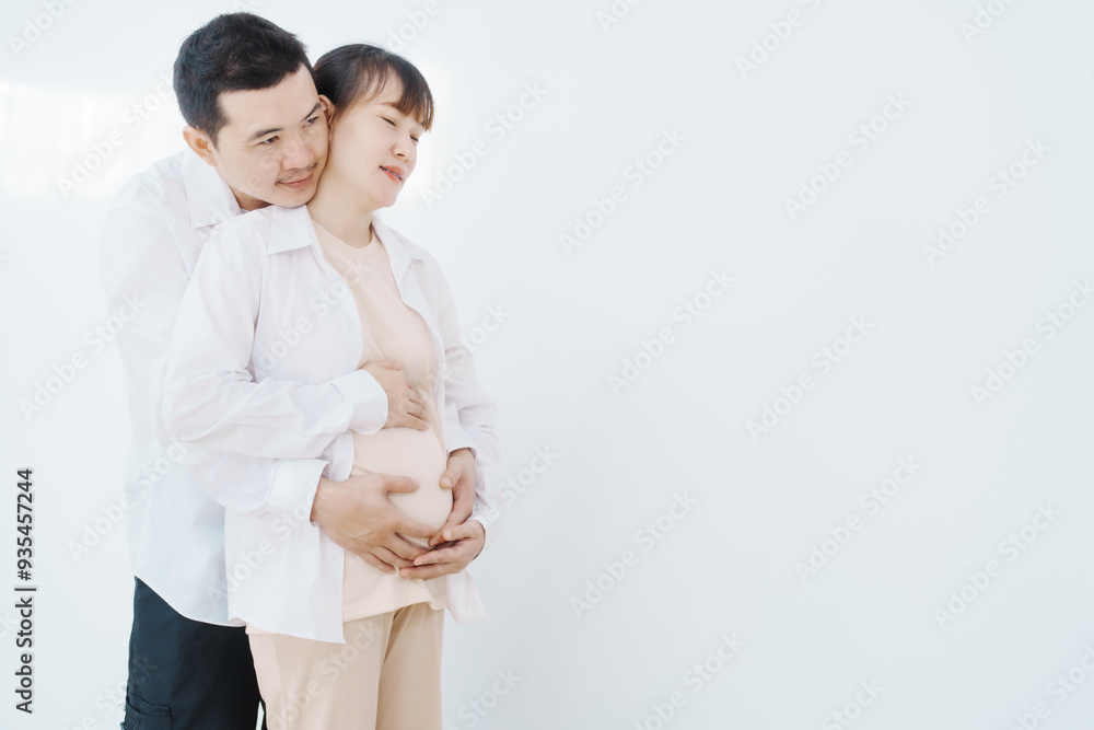 A happy Asian couple, expecting a baby, embraces in a cozy living room. The pregnant woman smiles warmly, while the man lovingly supports her, capturing a moment of joyful anticipation. A happy Asian couple, expecting a baby, embraces in a cozy living room. The pregnant woman smiles warmly, while the man lovingly supports her, capturing a moment of joyful anticipation.
