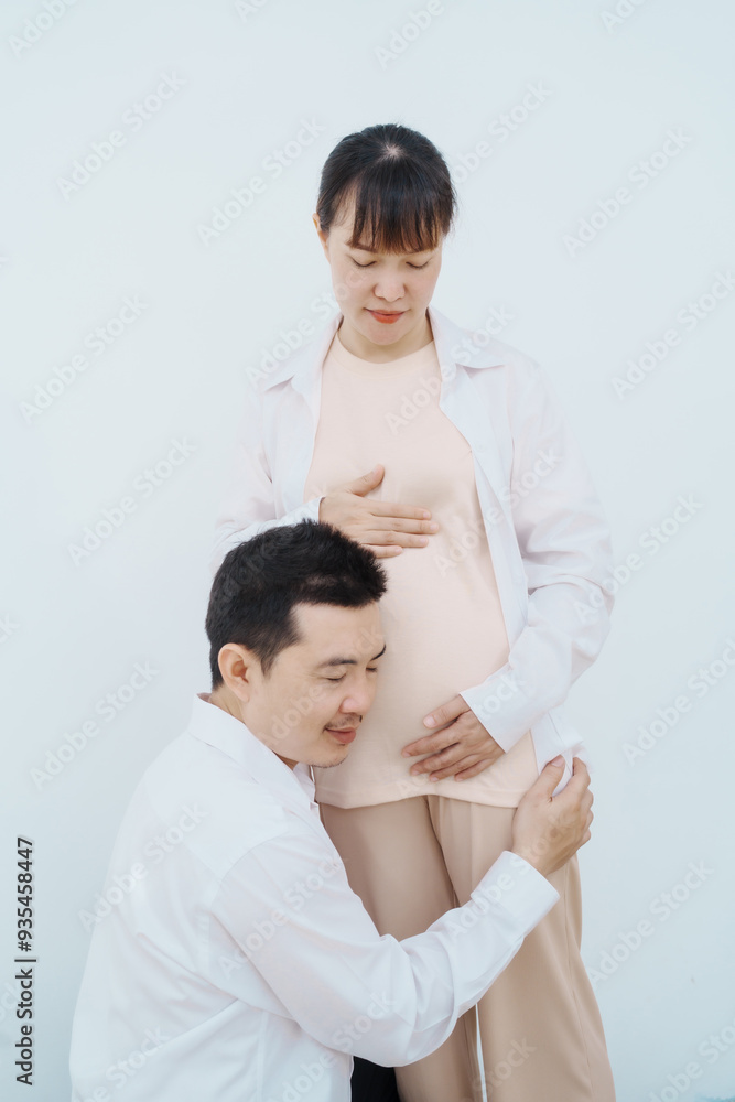 A happy Asian couple, expecting a baby, embraces in a cozy living room. The pregnant woman smiles warmly, while the man lovingly supports her, capturing a moment of joyful anticipation. A happy Asian couple, expecting a baby, embraces in a cozy living room. The pregnant woman smiles warmly, while the man lovingly supports her, capturing a moment of joyful anticipation.