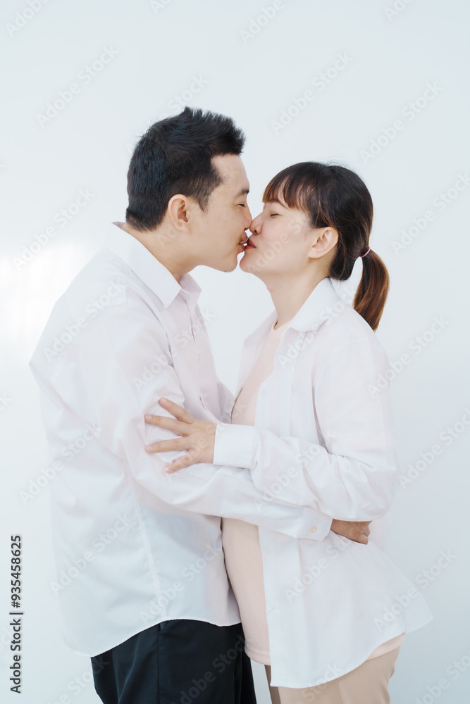 A happy Asian couple, expecting a baby, embraces in a cozy living room. The pregnant woman smiles warmly, while the man lovingly supports her, capturing a moment of joyful anticipation. A happy Asian couple, expecting a baby, embraces in a cozy living room. The pregnant woman smiles warmly, while the man lovingly supports her, capturing a moment of joyful anticipation.
