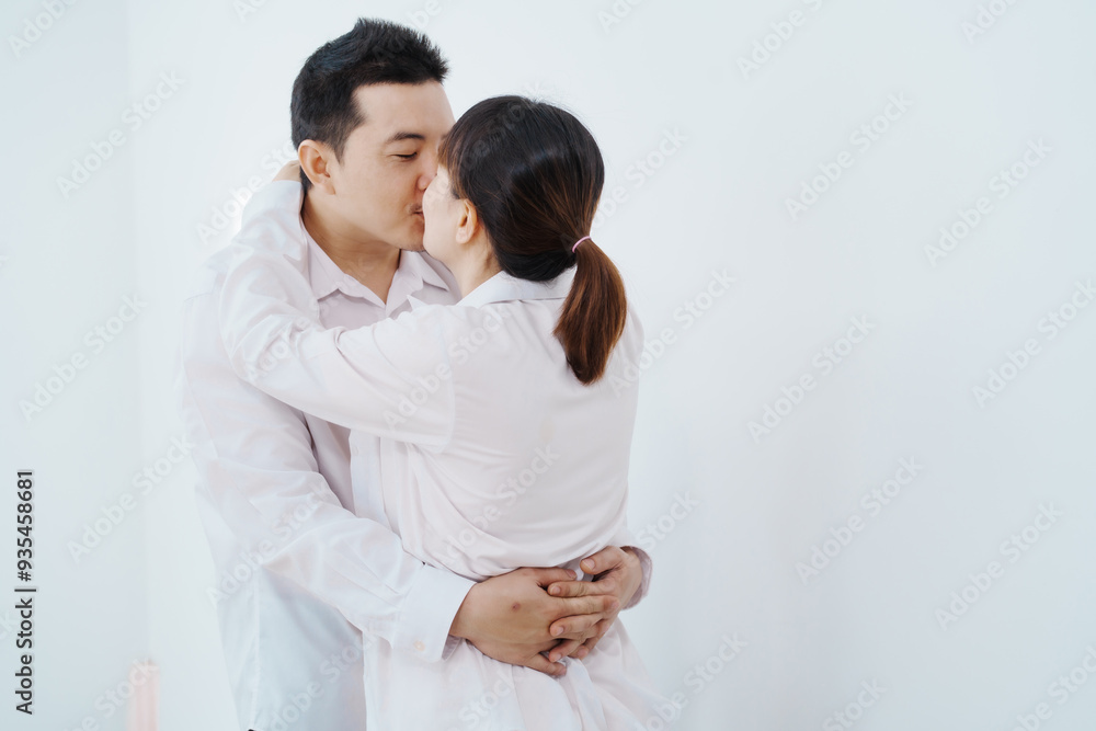 A happy Asian couple, expecting a baby, embraces in a cozy living room. The pregnant woman smiles warmly, while the man lovingly supports her, capturing a moment of joyful anticipation. A happy Asian couple, expecting a baby, embraces in a cozy living room. The pregnant woman smiles warmly, while the man lovingly supports her, capturing a moment of joyful anticipation.